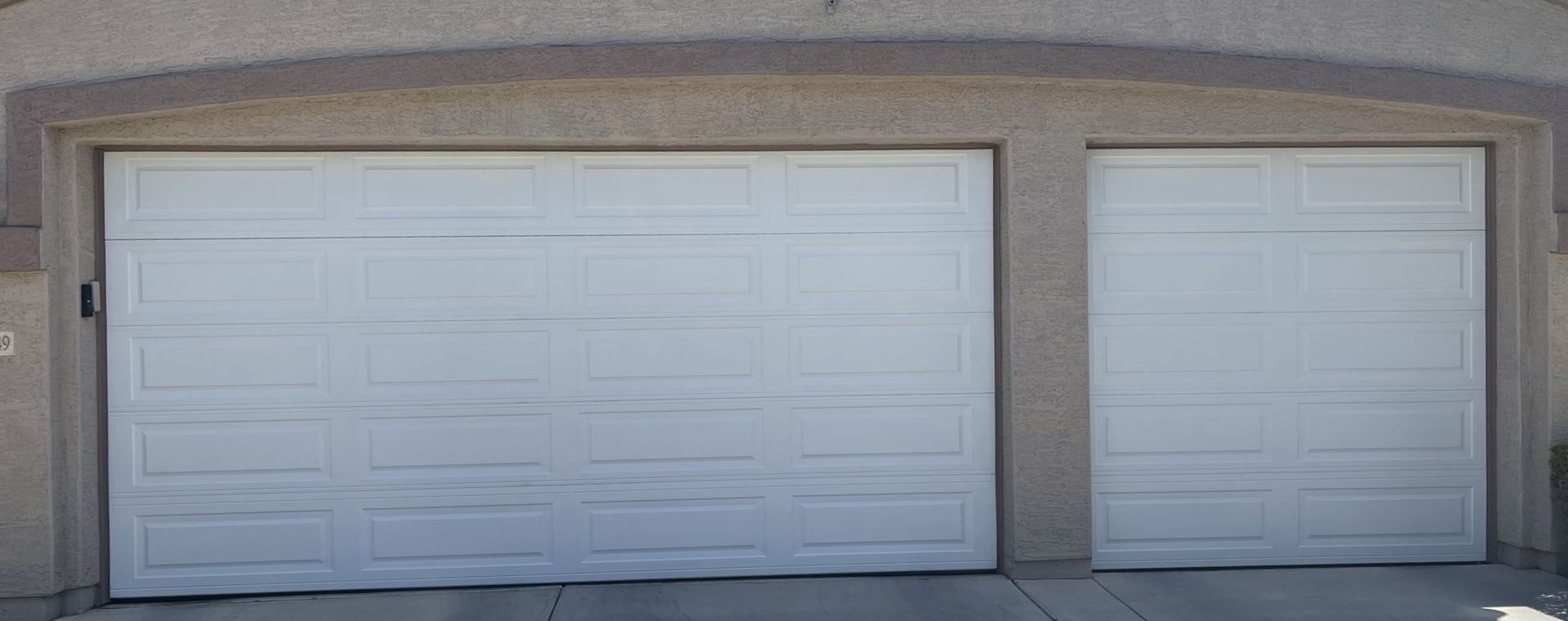 A white two-car garage with two paneled doors under a curved stucco archway.