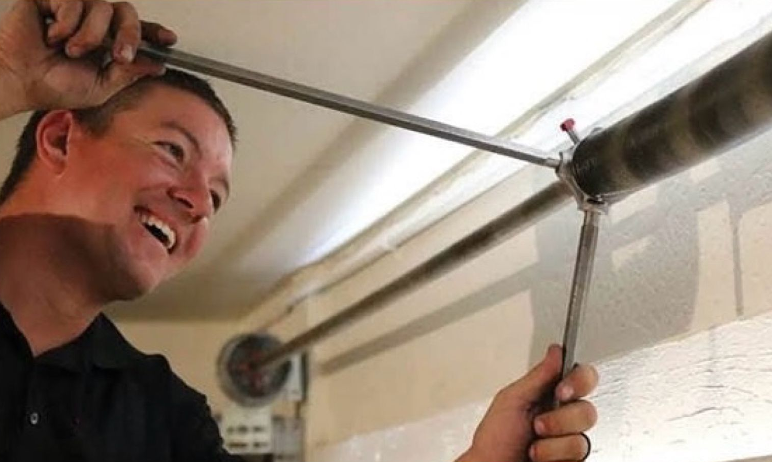 A professional adjusting a garage door torsion spring using a winding bar in a workshop setting.