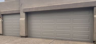 A wide-angle shot of a tan two-car garage with raised panel doors and a matching stucco exterior against a gravel driveway.