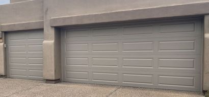 A wide-angle shot of a tan two-car garage with raised panel doors and a matching stucco exterior against a gravel driveway.