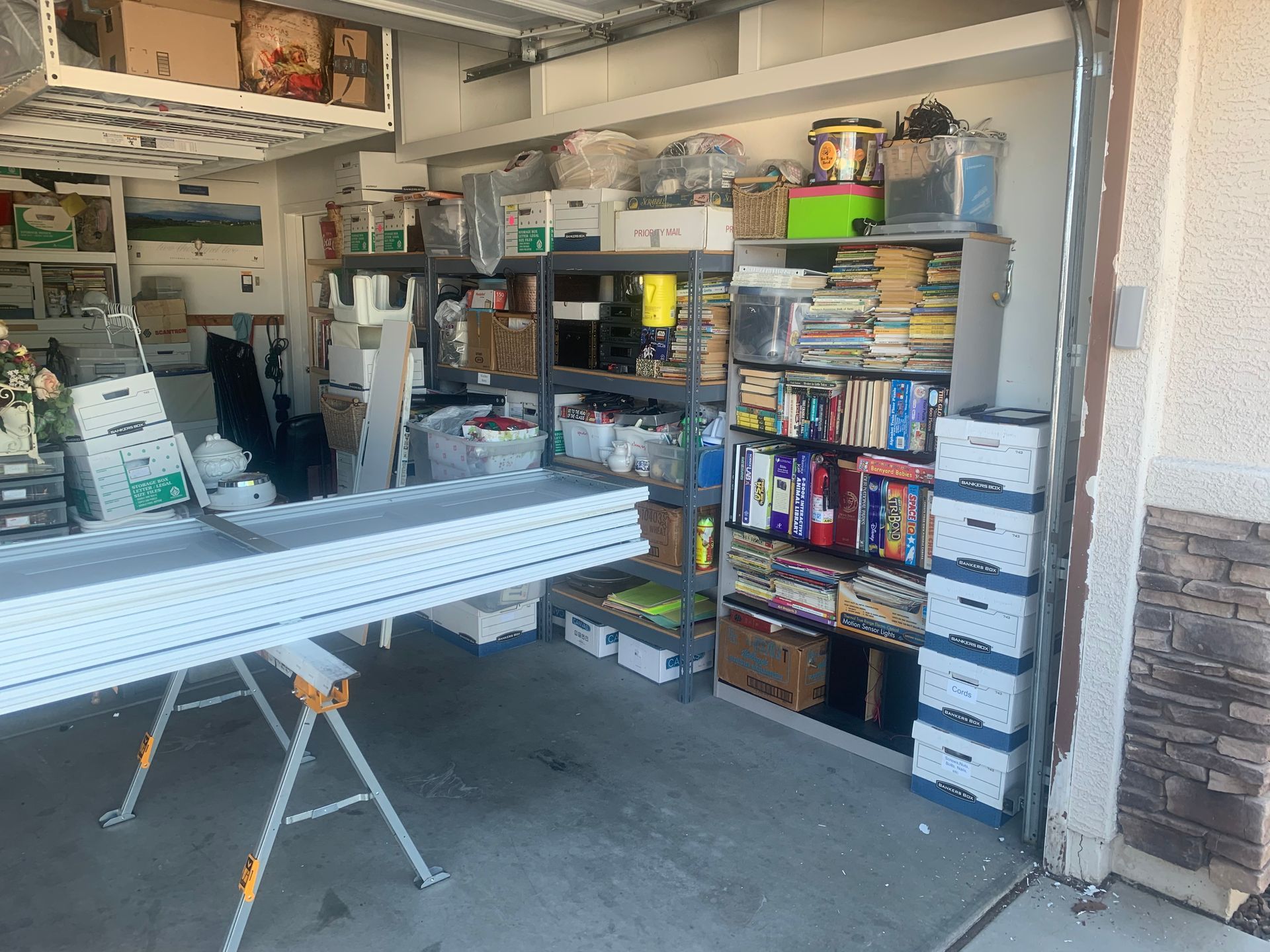 A garage storage area filled with shelves, cardboard boxes, and white planks resting on sawhorses.
