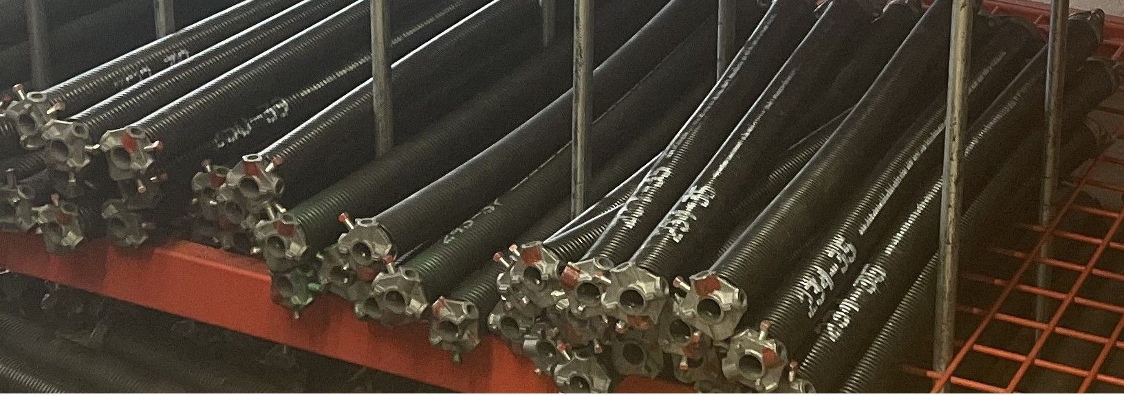 A rack filled with rows of cylindrical, black metal industrial parts with metal connectors at the ends.