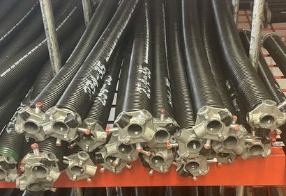 A collection of black metal garage door torsion springs with cast aluminum winding cones arranged on a rack.