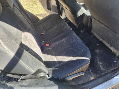 Back seat of a car with a worn dark fabric seat and sunlight on the upholstery