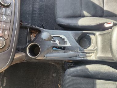 Car center console with manual gear shift, cup holders, and storage compartment, black interior.