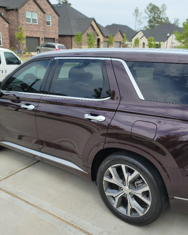 Maroon SUV parked in a suburban driveway, side view with a brick house in the background