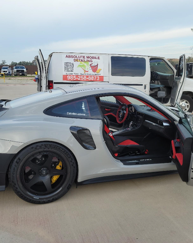 Silver sports car with open driver door parked beside a white van at an outdoor lot