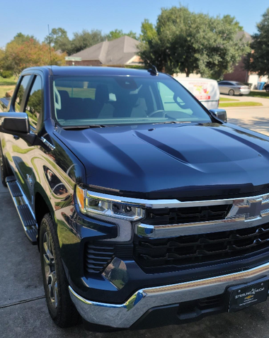 Black Chevrolet Silverado parked in a sunny suburban driveway with houses and trees in the background