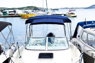 White boat with blue canopy docked at a marina, surrounded by other boats on calm water