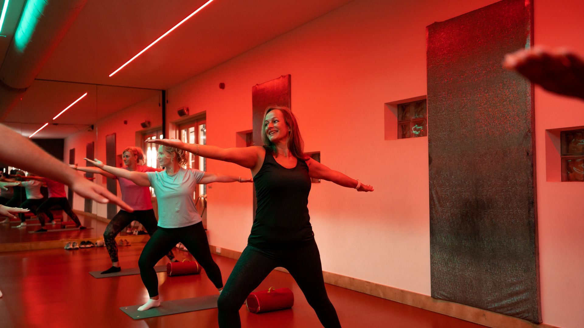 Mensen die een dansworkout doen in een rood verlichte sportschool met spiegelwanden.