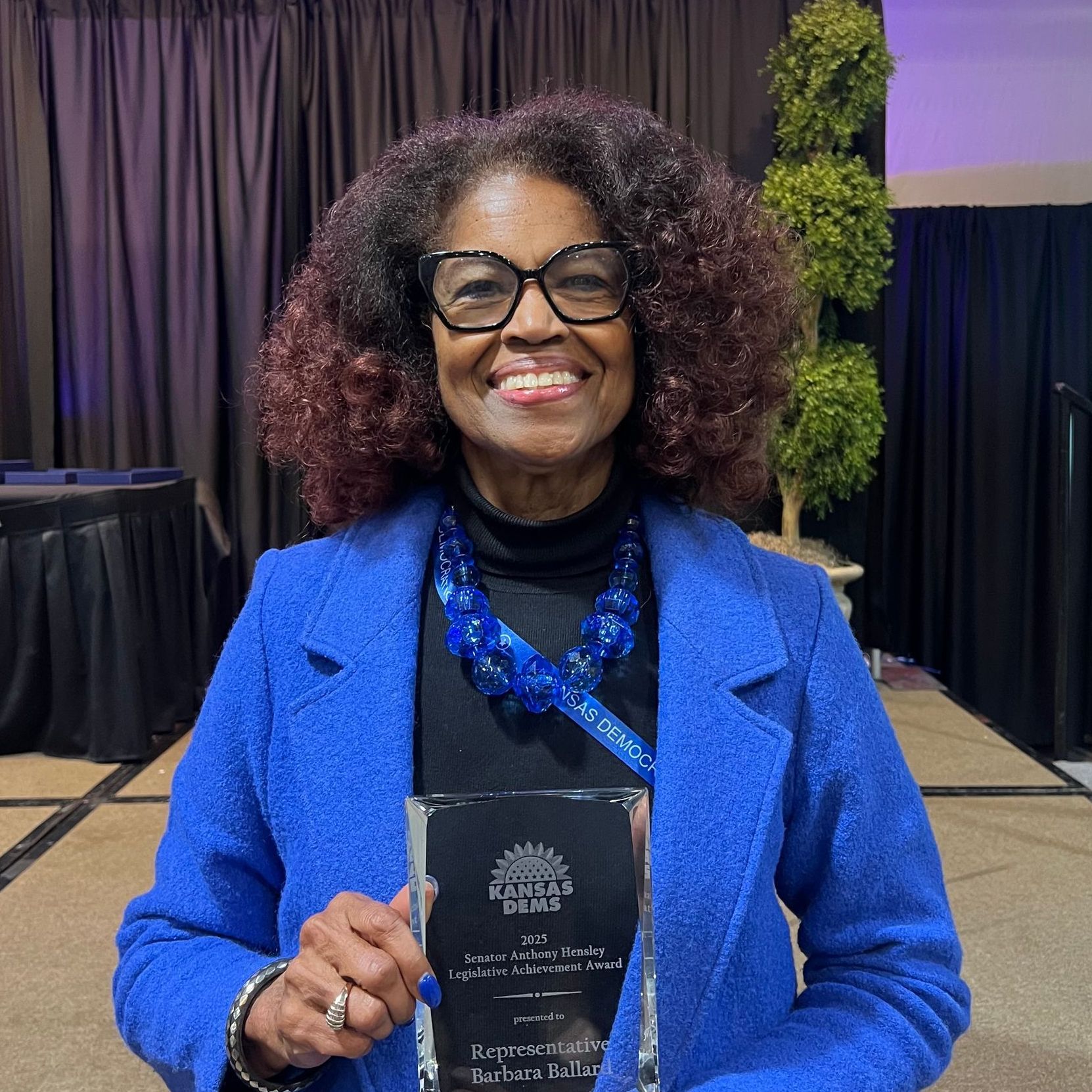 A woman in a blue coat is holding a trophy and smiling.