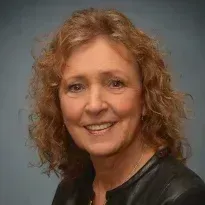 A woman with curly hair and a black jacket is smiling for the camera.