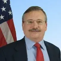 A man in a suit and tie is standing in front of an american flag.