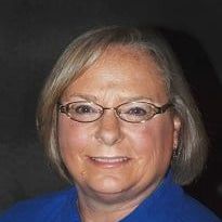 A woman wearing glasses and a blue shirt is smiling for the camera.