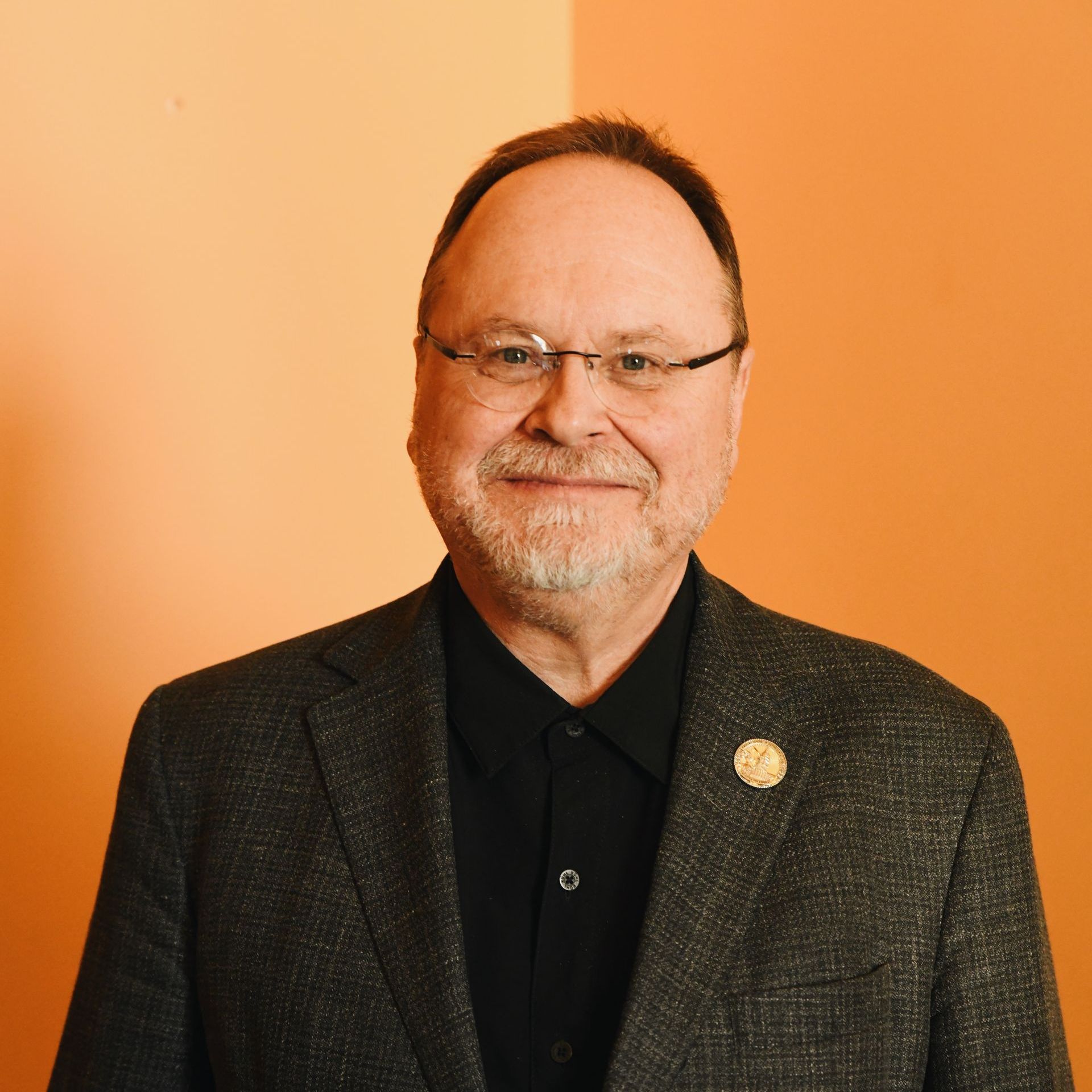 A man with glasses and a beard is wearing a suit and a black shirt.