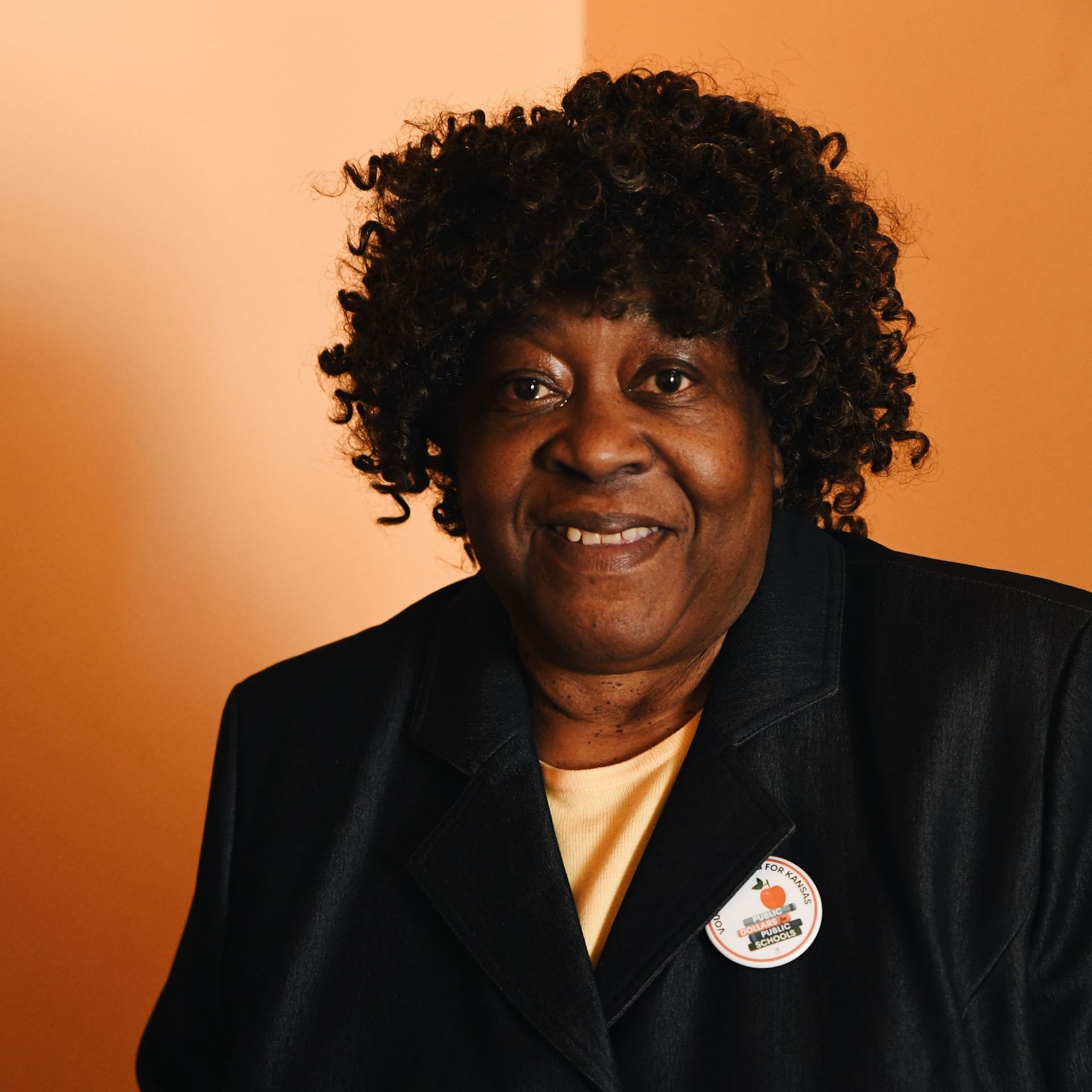 A woman with curly hair is smiling and wearing a black jacket