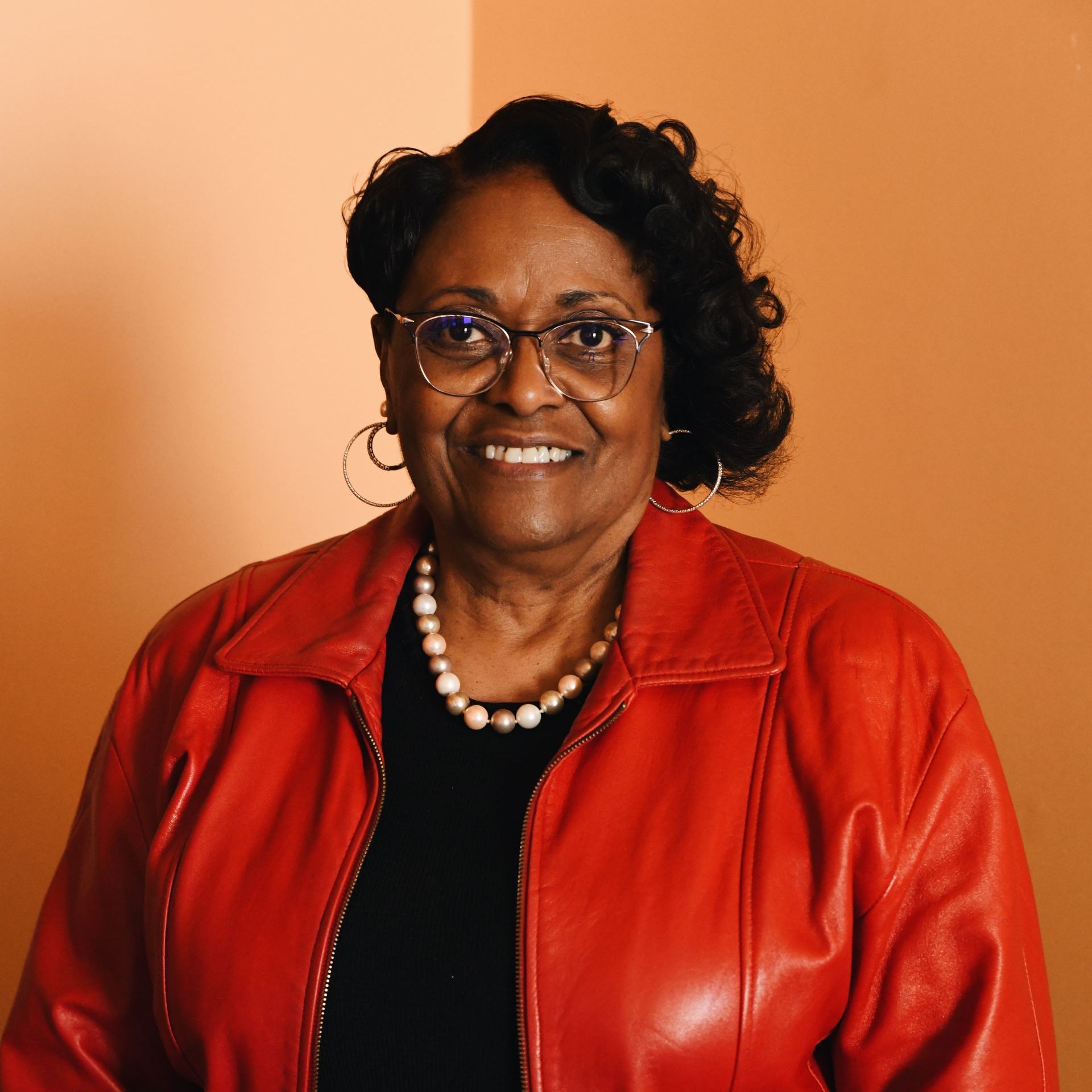 A woman wearing glasses and a red jacket is smiling for the camera.