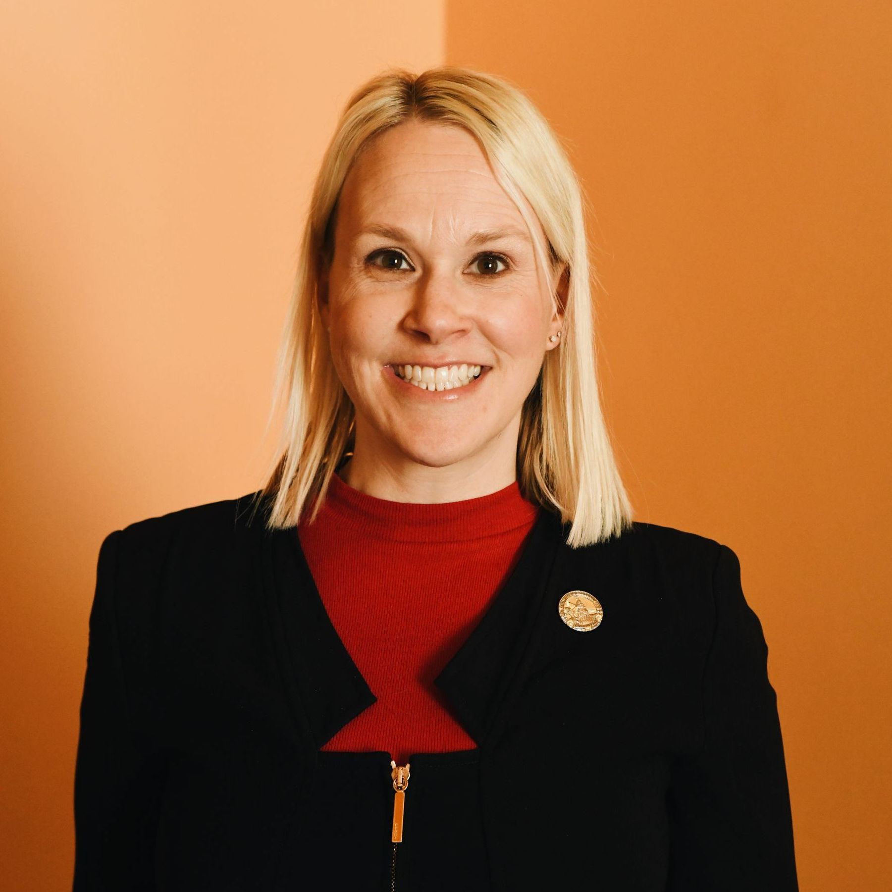 A woman wearing a black jacket and a red sweater is smiling for the camera.