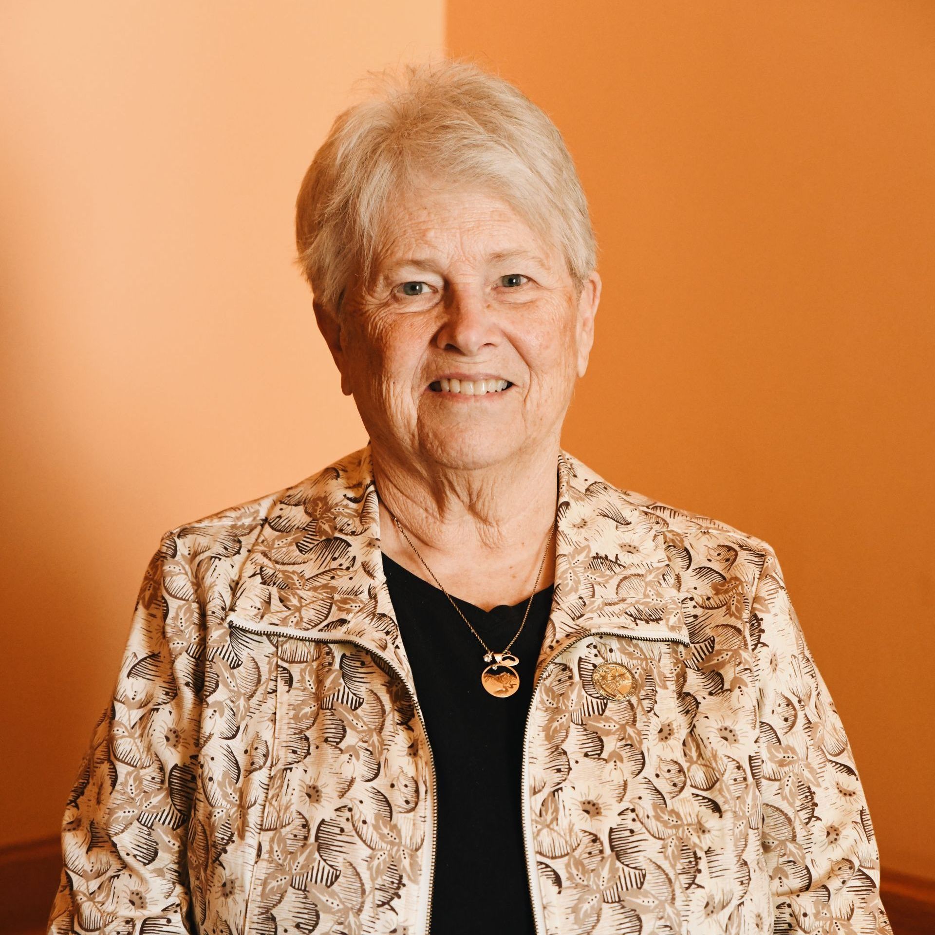 An older woman wearing a jacket and a necklace is smiling for the camera.