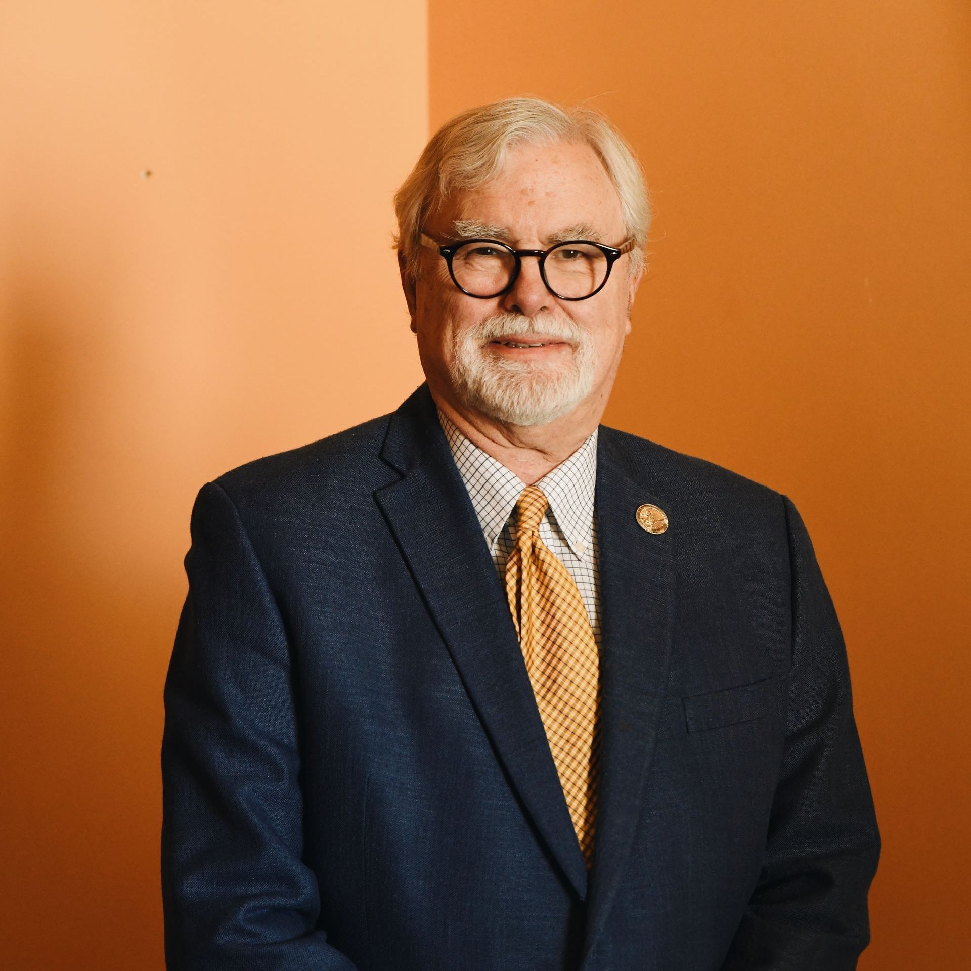 A man in a suit and tie is standing in front of an orange wall.