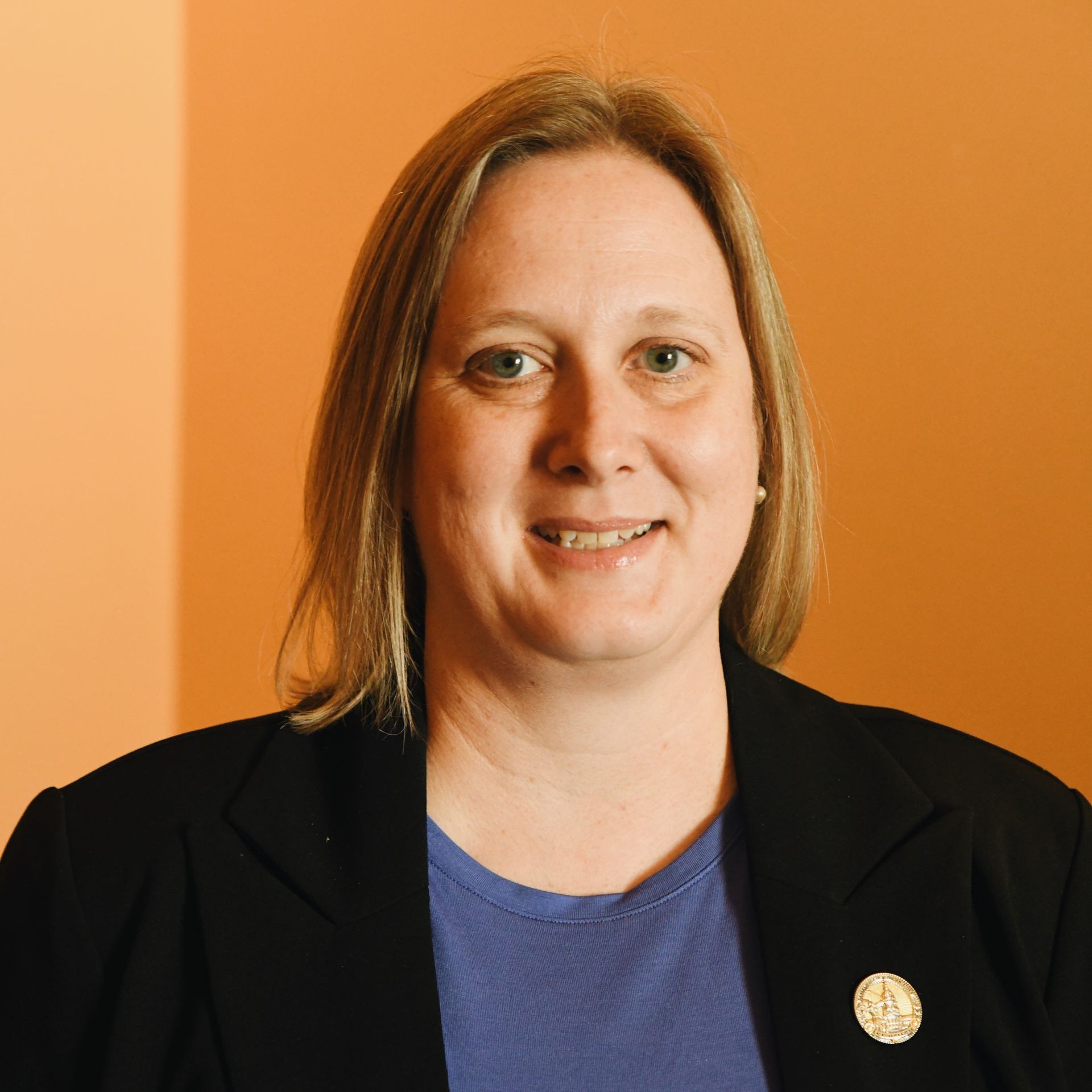 A woman wearing a black jacket and a purple shirt is smiling for the camera.