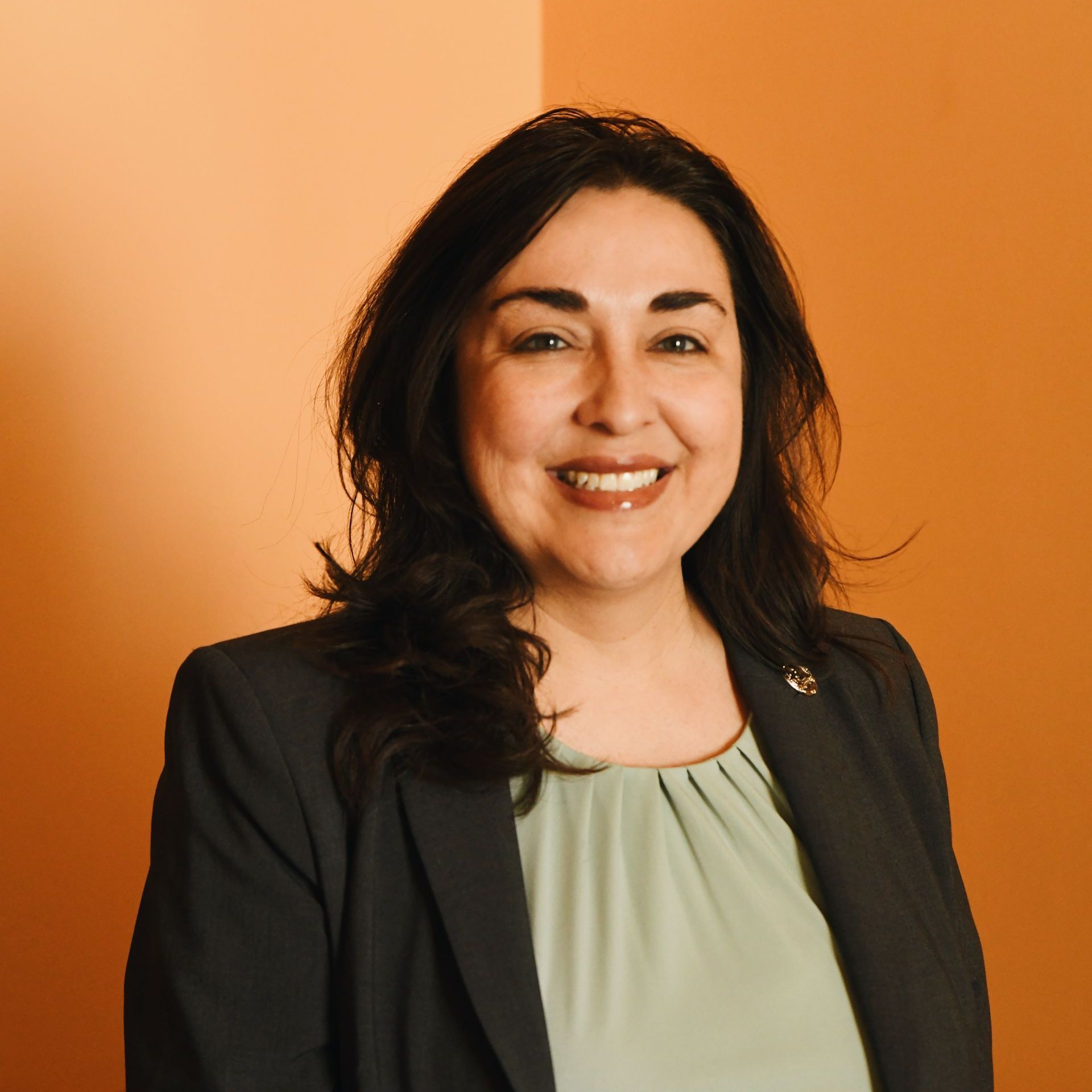 A woman wearing a black jacket and a green shirt smiles for the camera