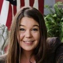 A woman is smiling in front of an american flag.