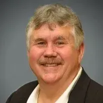 A man with a mustache is wearing a suit and smiling for the camera.