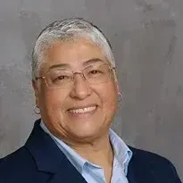 A woman wearing glasses and a blue jacket is smiling for the camera.