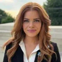 A woman with long red hair is wearing a black jacket and white shirt.