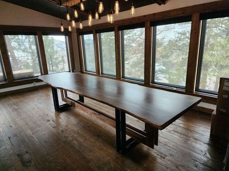 A long wooden table is sitting in a room with lots of windows.