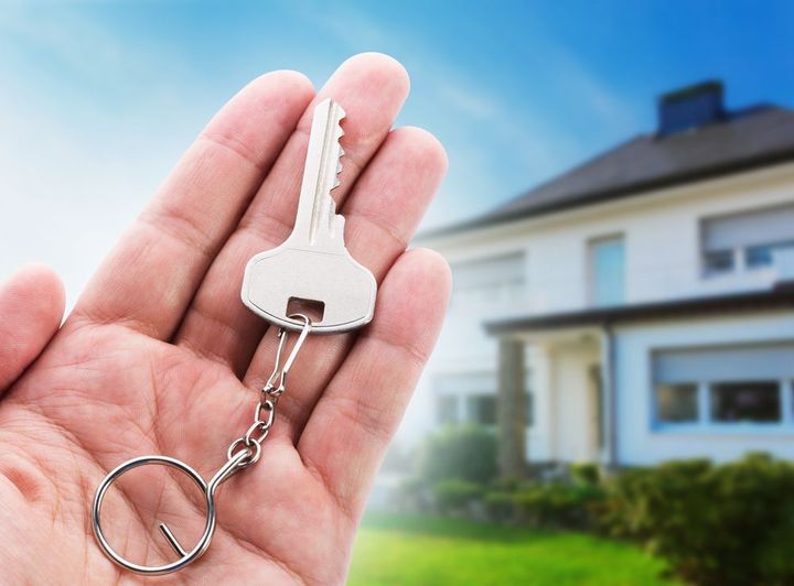 A person is holding a key in front of a house.