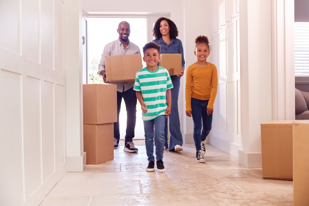 A family is moving into a new home carrying cardboard boxes.