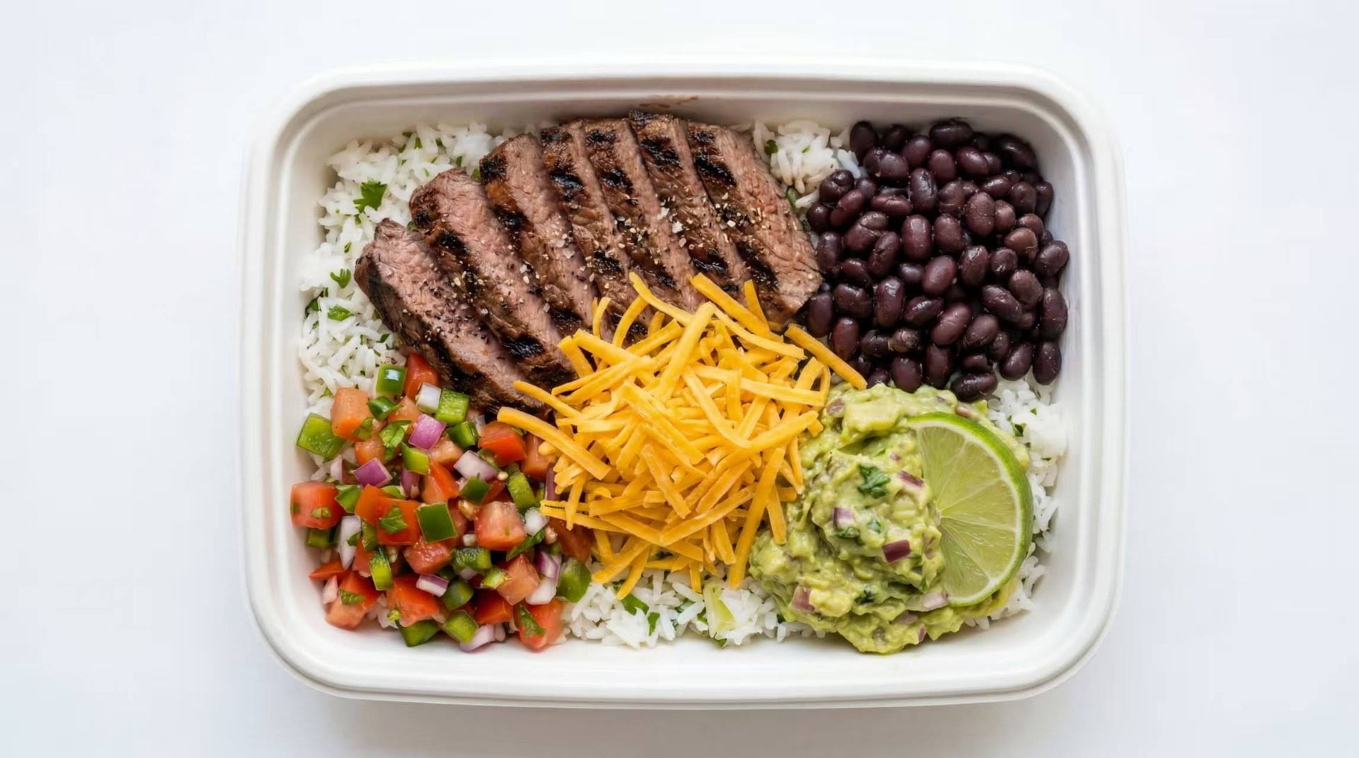 Meal prep container with grilled sliced steak, black beans, pico de gallo, shredded cheese, and guacamole on lettuce