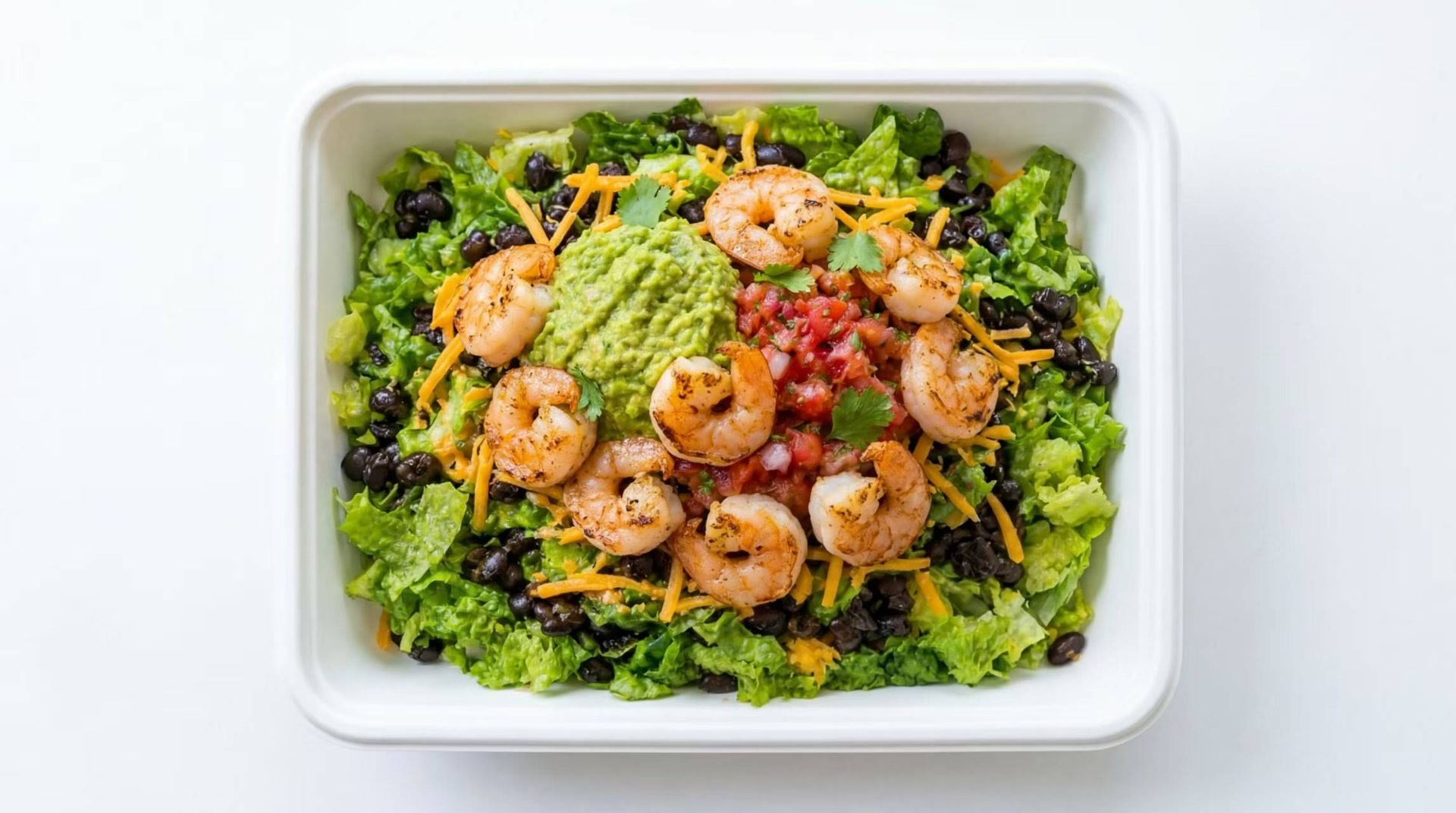Shrimp salad with avocado and cherry tomatoes on a bed of greens in a white container