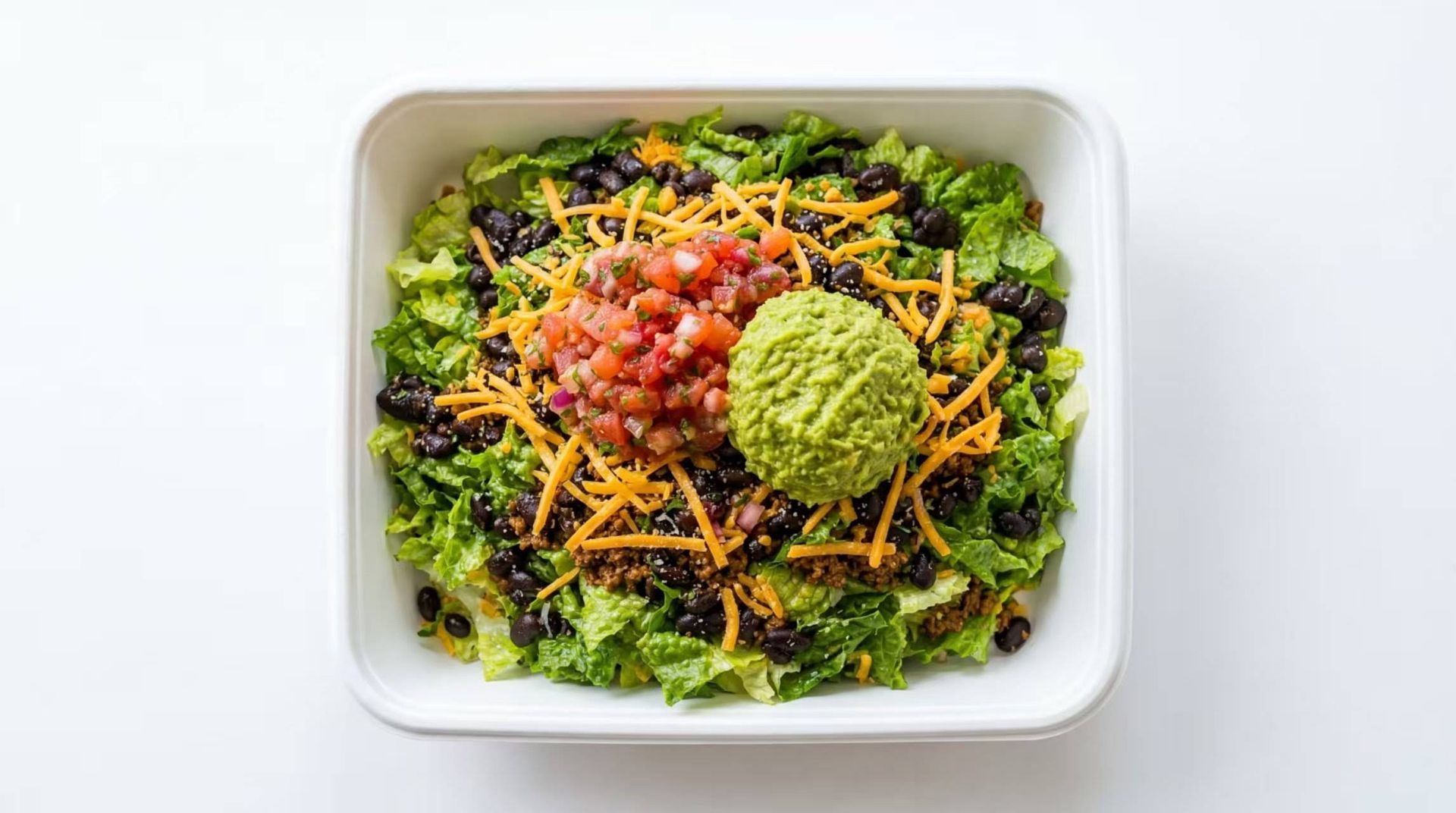 Top-down view of a salad bowl with leafy greens, tomatoes, shredded carrots, and two vegetable toppings