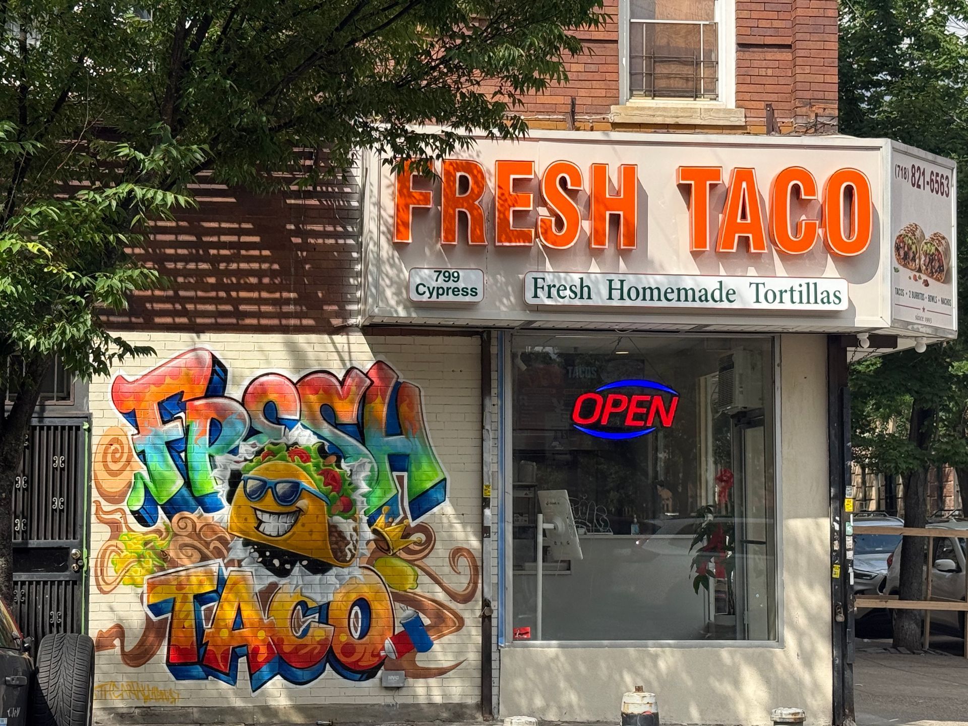 Fresh Taco storefront with graffiti mural and neon OPEN sign on a city street