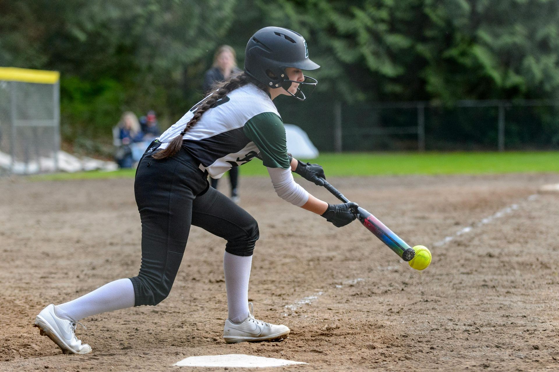 Softball player in uniform swings a bat, preparing to hit the ball on a field.
