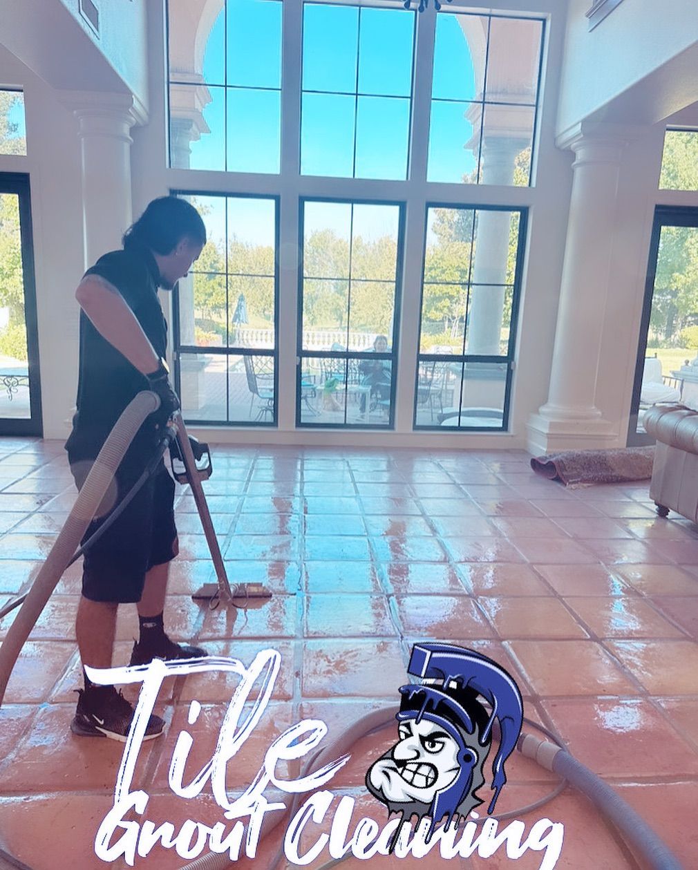 Man cleaning tile floor with equipment in a bright room with large windows.