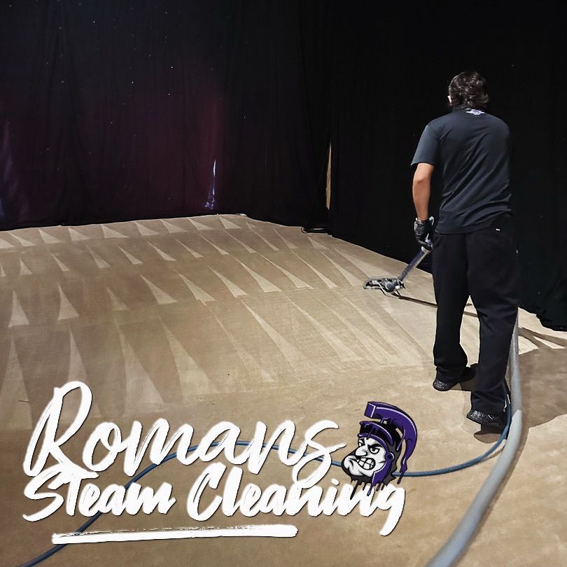 Man steam cleaning a large beige carpet in a dark room. Romans Steam Cleaning logo is visible.