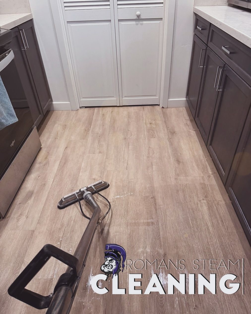 Steam cleaner on light wood-look floor in kitchen with dark cabinets, white doors.