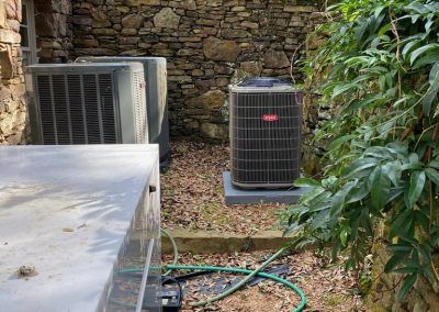 A row of air conditioners are sitting next to each other in a backyard.