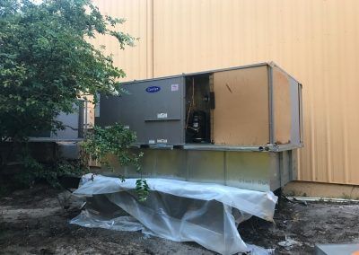 A large air conditioner is sitting on top of a pile of dirt in front of a building.