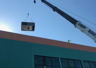 A crane is lifting a piece of equipment from the roof of a building.