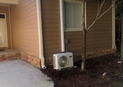A white air conditioner is sitting on the side of a house next to a window.