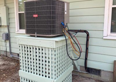 An air conditioner is sitting on top of a white box on the side of a house.