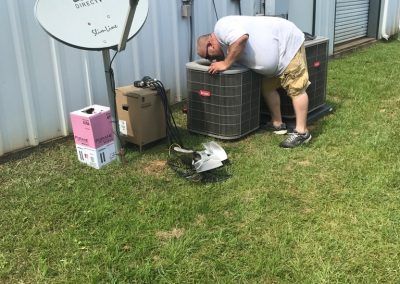 A man is laying on the grass next to an air conditioner and a satellite dish.