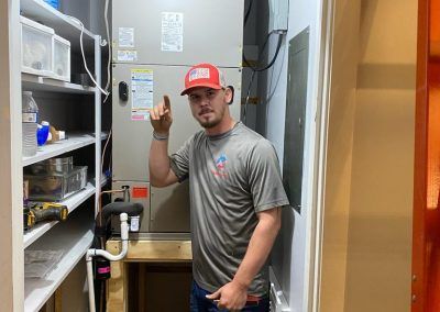 A man in a red hat is standing in a closet next to an air conditioner.