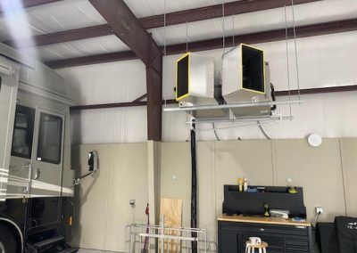 A rv is parked in a garage with heaters hanging from the ceiling.