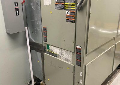 A large air conditioner is sitting in a room next to a broom.